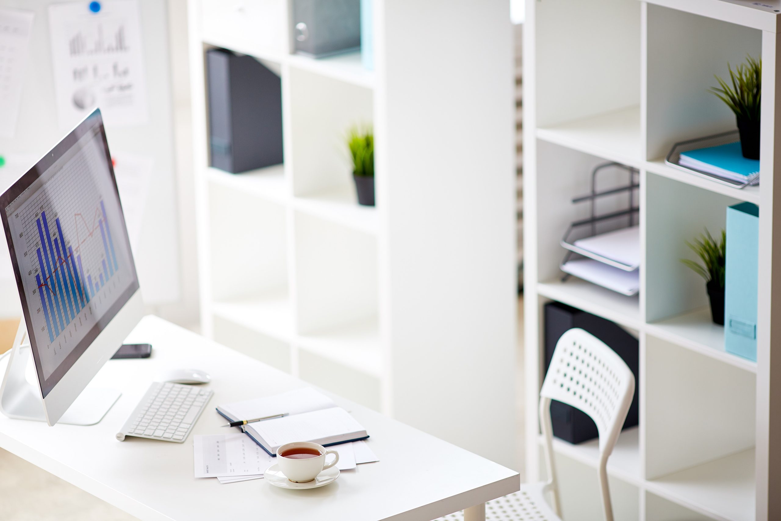 Workplace of banker with computer monitor, keypad, notebook and cup of tea